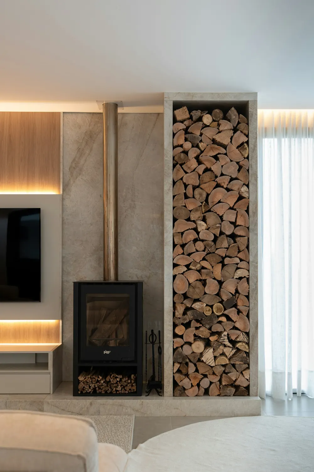 Poêle à bois moderne contre un mur de béton, avec une niche remplie de bûches