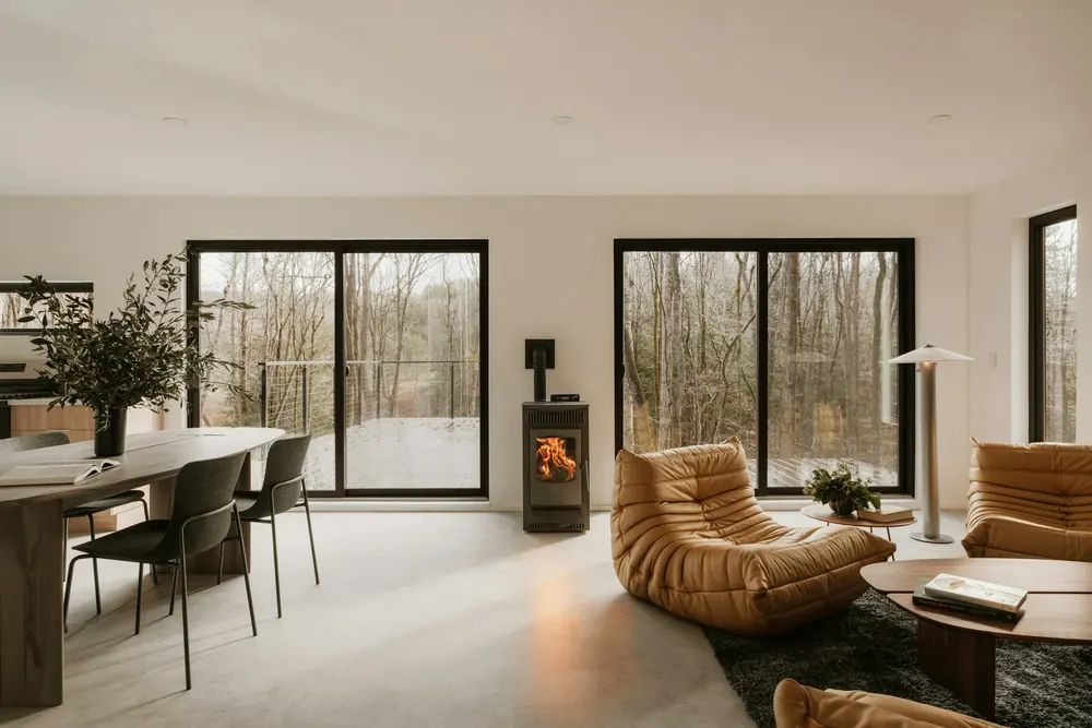 Salon contemporain blanc avec baies vitrées sur la forêt et poêle à granulés
