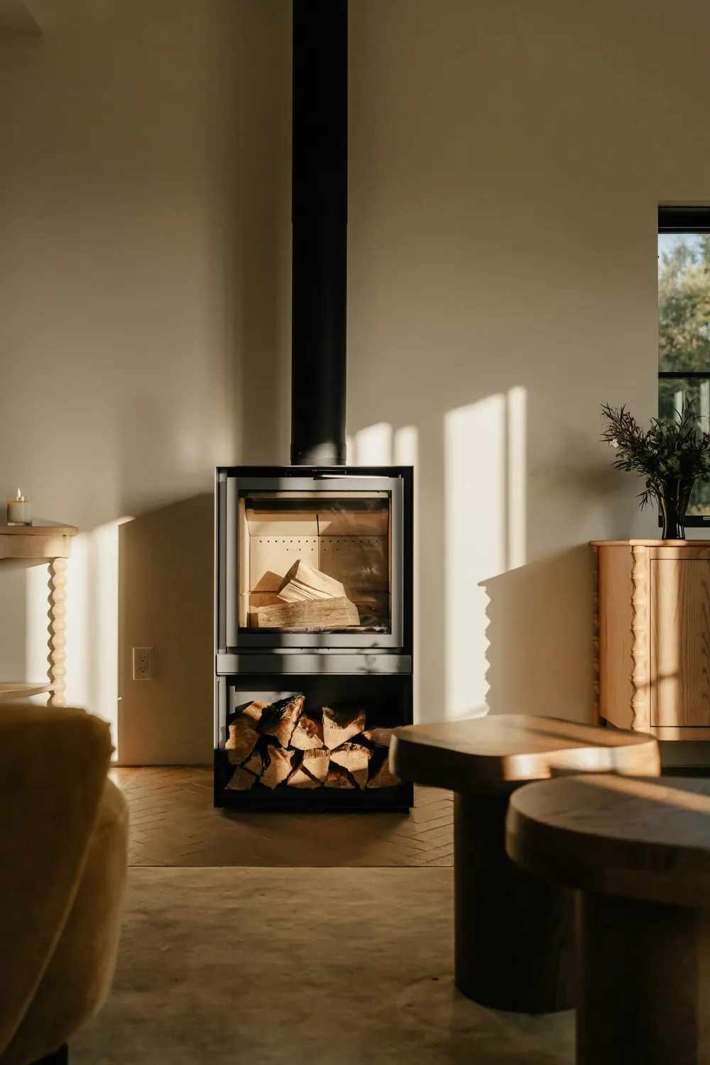Poêle à bois contemporain avec sa réserve de bûches, dans un salon baigné de soleil